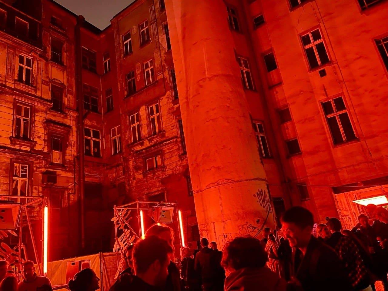 Historischer Innenhof vollständig in rotes Licht getaucht, mit Gästen und Lichtobjekten