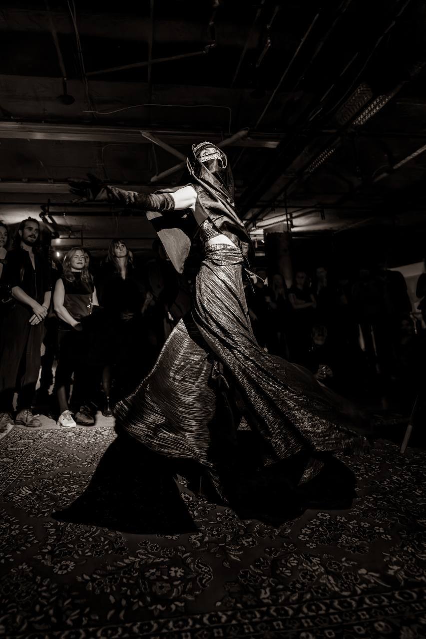 Eine Tänzerin im fließenden Goldkleid vor den Gästen im rohen Raum